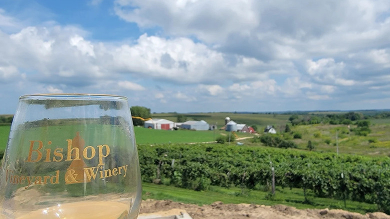A wine glass from Bishop Vineyard and Winery in front of bucolic farm in Sherrill, Iowa
