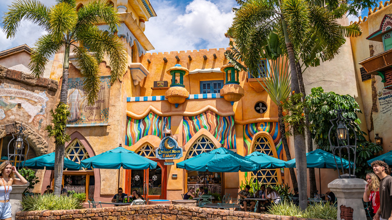 Exterior of Croissant Moon Bakery Cafe at Universal's Islands of Adventure with palm trees and bright blue umbrellas over outdoor seating.