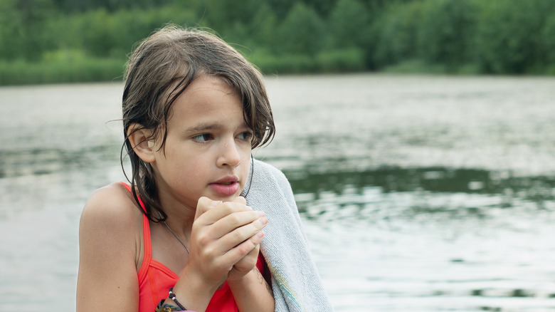A girl shivering on a lake with a towel around her