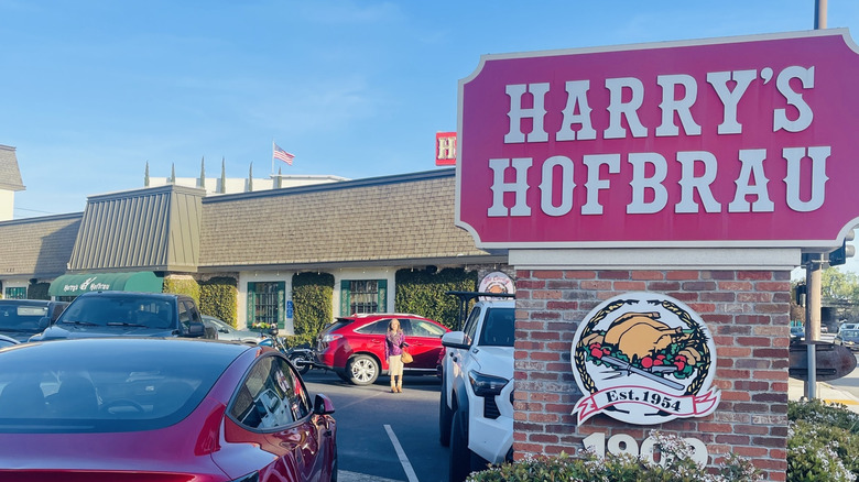Exterior of Harry's Hofbräu with a sign outside and cars parked in the lot
