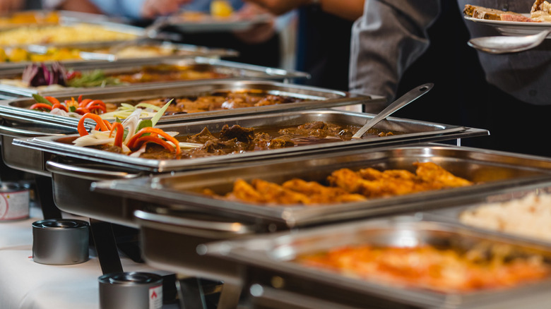 A line of hold hot metal trays filled with food on a cafeteria line