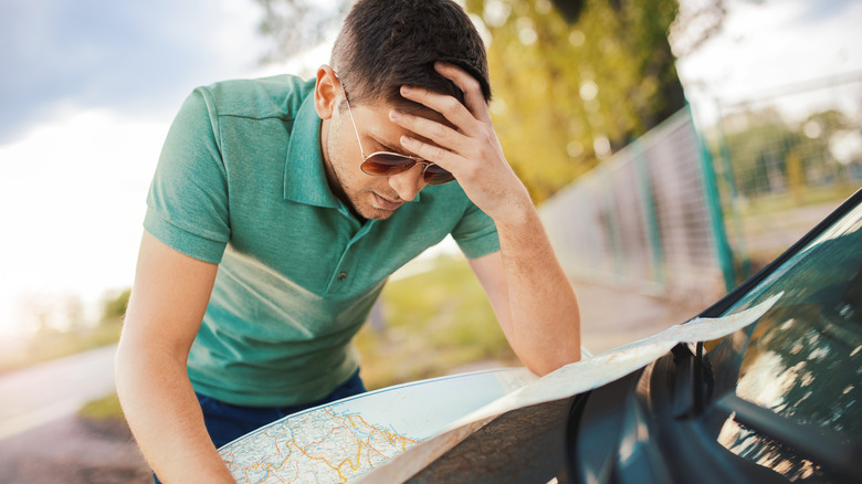 Man leaning on a car hood looking at a map with his head in his hand
