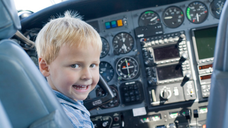 Child looking back over his shoulder at the camera, whilst sat in a leather seat of a cockpit in a plane