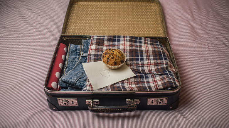 View of a muffin with a note underneath it, on top of a suitcase, on a bed