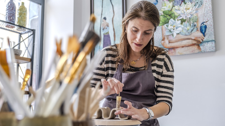 Middle-aged caucasion lady working on pottery surrounded by tools and artwork