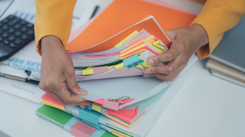 A person looking through a pile of papers organized with clips and colorful paper