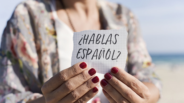 Woman holding a piece of paper with a question in Spanish.