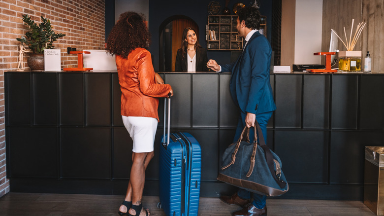Man and woman with luggage talking to reception staff at a hotel