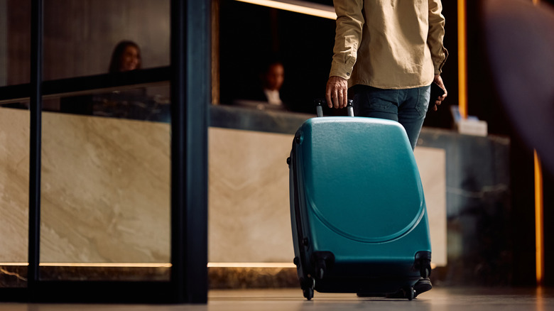 Man dragging blue suitcase toward hotel check-in counter