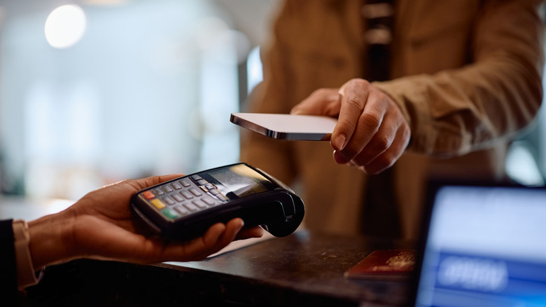 Man tapping phone on card machine at hotel check-in