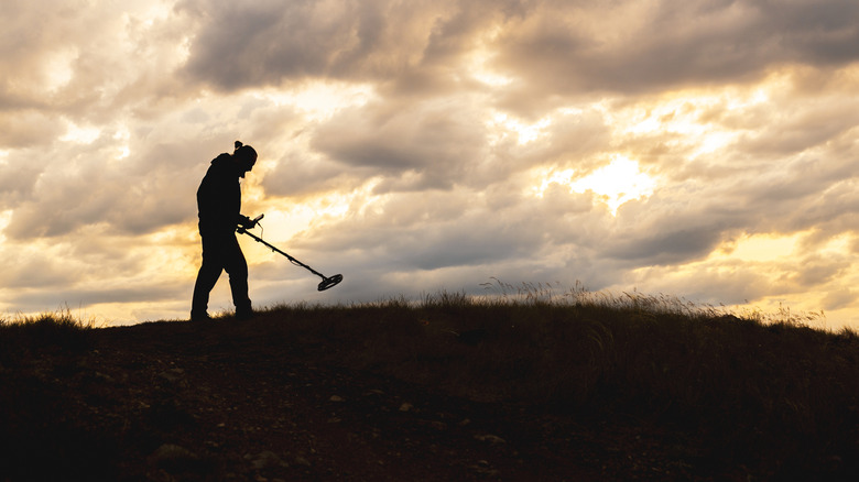 A silhouette of a man walking on a hill with a metal detector in his hand