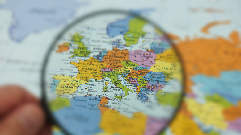 Hand holds a magnifying glass over a colored map of Europe