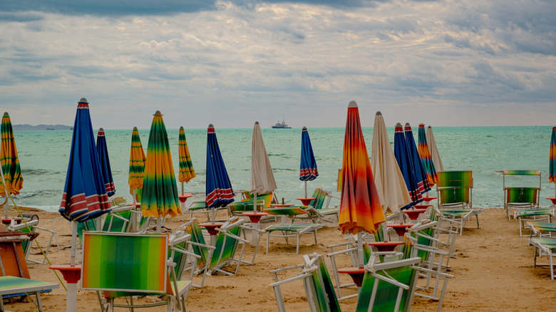 Colorful folded beach umbrellas leaning against beach loungers on an empty sandy beach