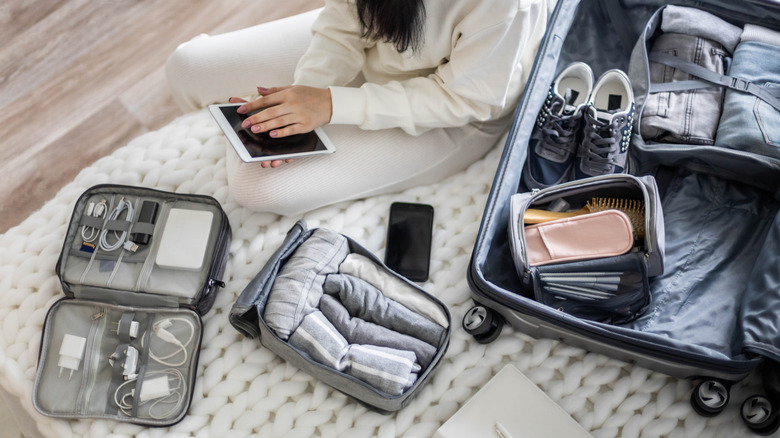 Top shot of open suitcase with packing cubes and clothes rolled up, woman sitting next to it