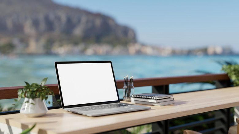 Photo of laptop and books on a table overlooking body of water and hillside