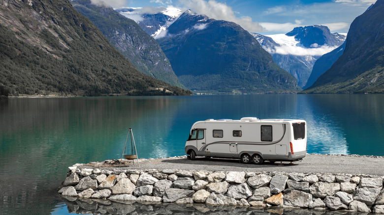 A large motorhome parked on a pier next to a mountain lake