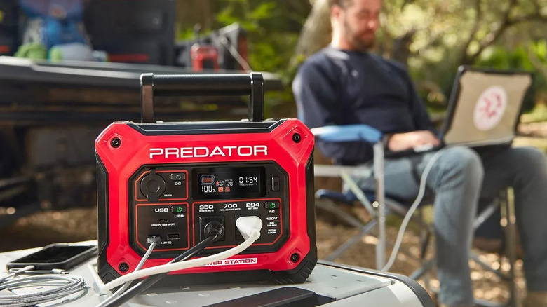 A man at a campsite works on his computer in the background with devices hooked up to a Predator brand power station
