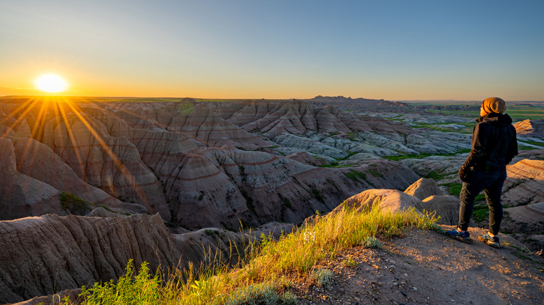 Hiker enjoying a vibrant sunrise over Panorama Point's rock formations in Badlands National Park