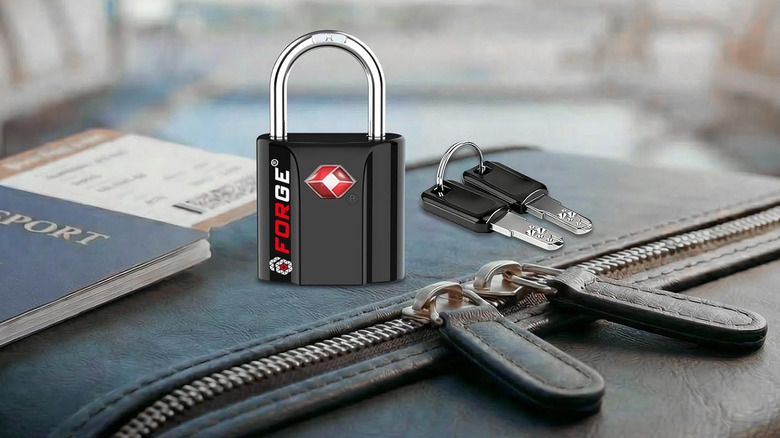 A Forge OX TSA-Approved Key Lock sitting on luggage next to its keys and a passport.