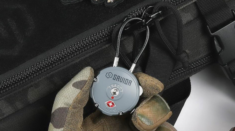 A gloved hand holding the Savior Equipment TSA-Approved 3-Digit Combination Cable Lock.