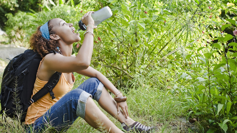 A hiker drinks water from a reusable plastic water bottle