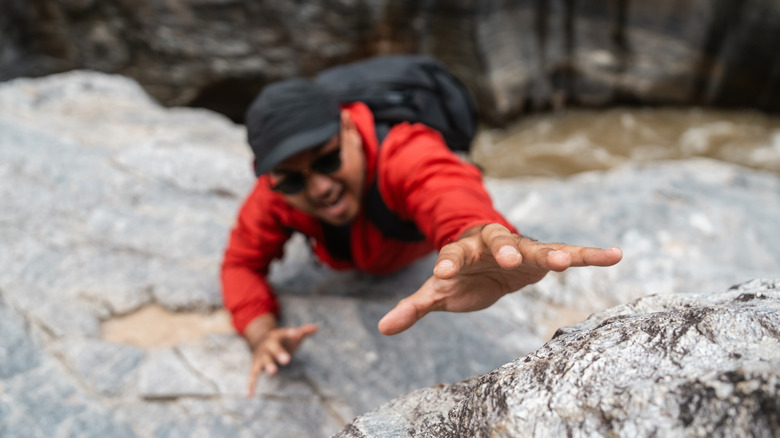 A hiker grasps for a hold on a steep cliff