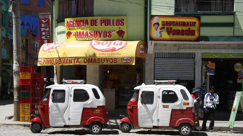 Tuk tuk taxis outside a shop with a yellow and red awning in La Paz, Bolivia