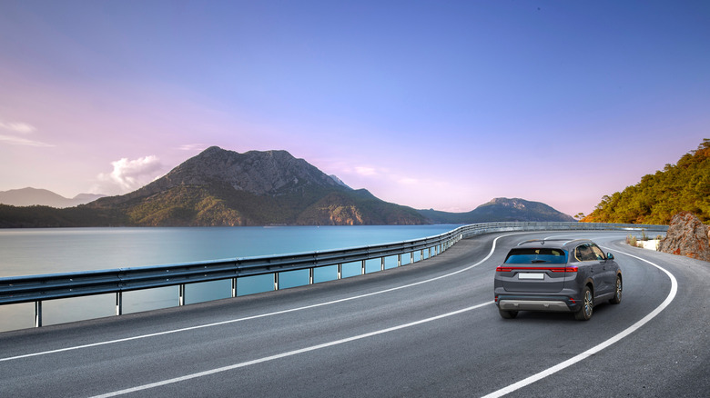 Car driving on a road with water and mountains on either side