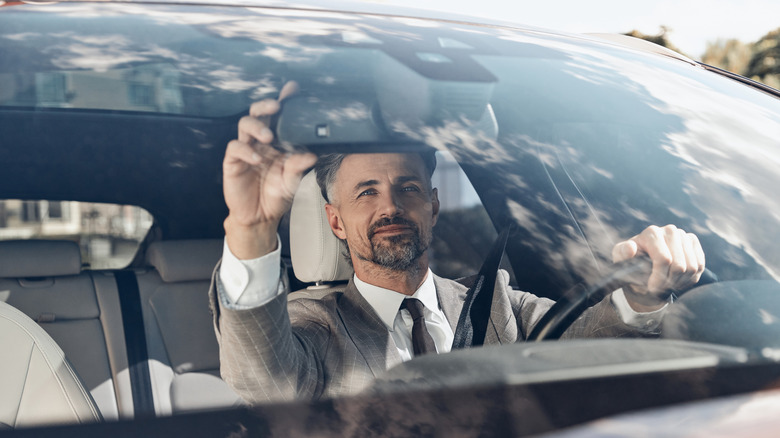Man in a suit adjusting a rear view mirror in a car
