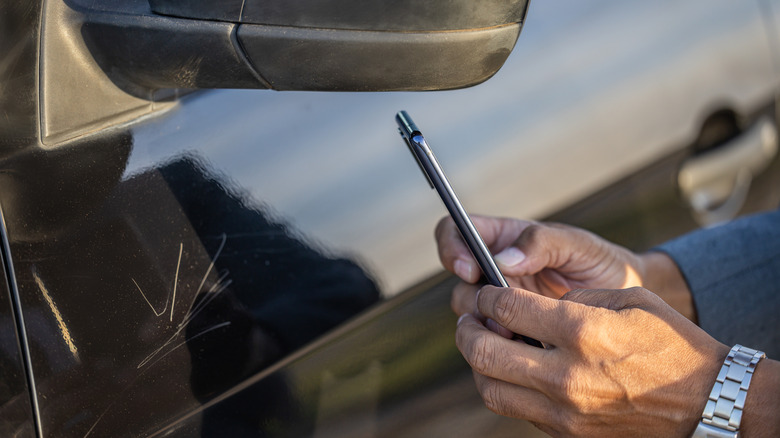 Hand holding phone, taking photo of scratch on car