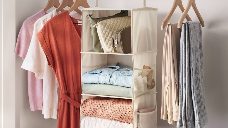 A three-shelf hanging closet organizer in a closet with clothes and shoes