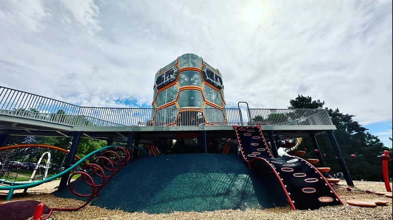 Orange and metal play structure in a treed, grassy park, Paco Sanchez Park, Denver