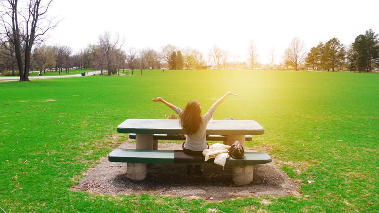 Woman throws her arms out in the sun in Washington Park, Denver