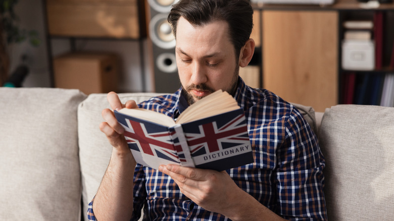 A man reads an English dictionary while sitting on the couch
