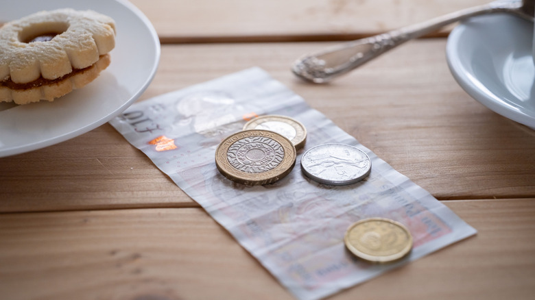 British pound sterling banknotes and coins on table with a cookie on a plate