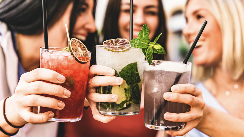 Three women clinking glasses of craft cocktails