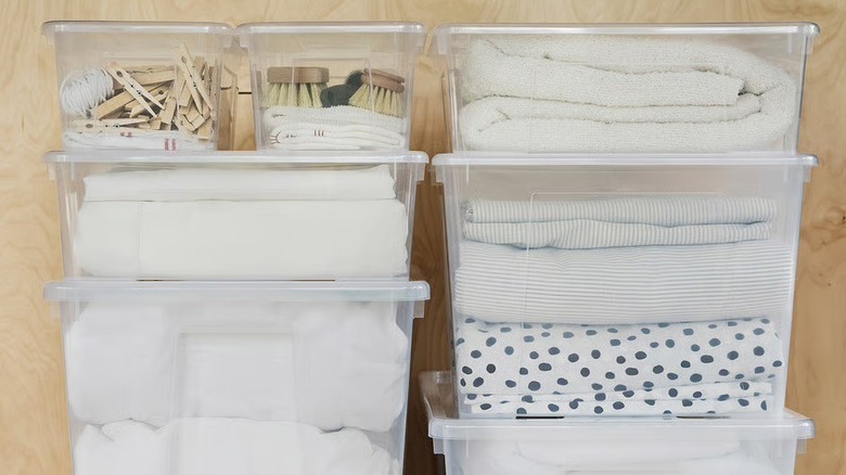 Two stacks of clear plastic bins filled with linens and laundry-related items