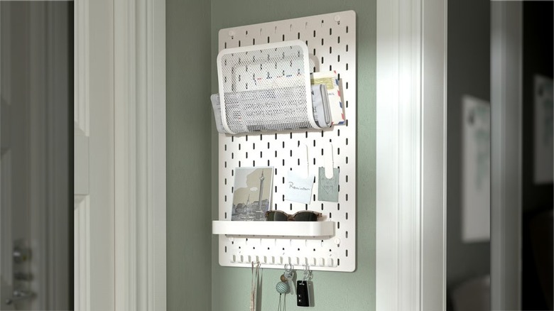 A pegboard shelf with trays and items stored on it, on a light green wall