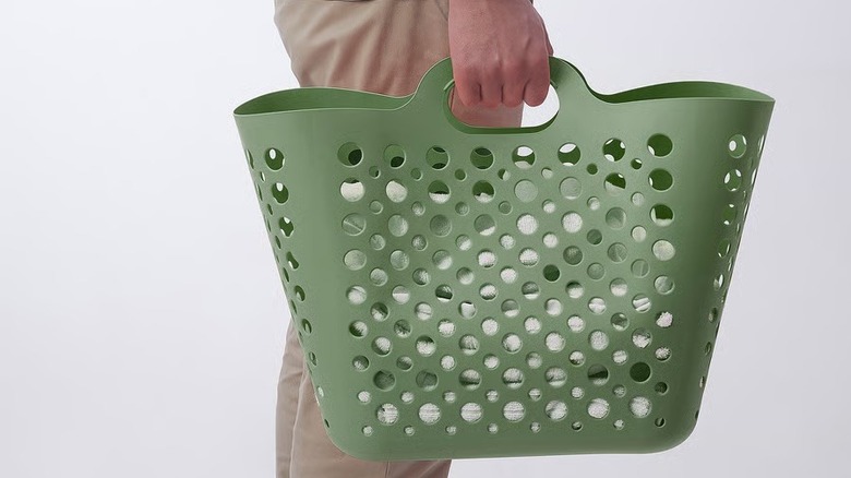A person in a neutral outfit holds a flexible green laundry basket