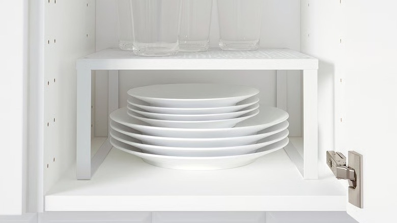 A small white shelf in a cabinet with glasses and plates