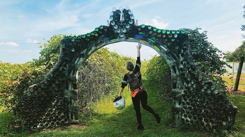 a person under an archway made of recycled wine bottles in a vineyard