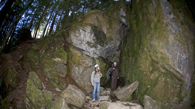 two people wearing helmets in front of the entrance of a cave in the dark