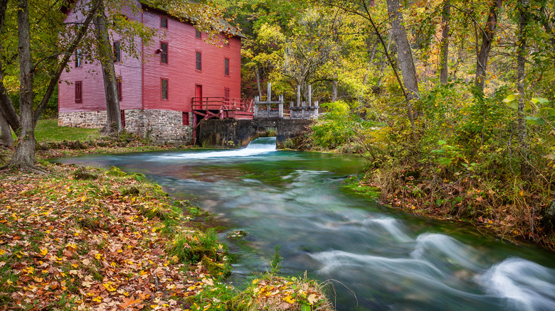 Historic red mill and water wheel near a creek in an autumnal forest, Ozarks