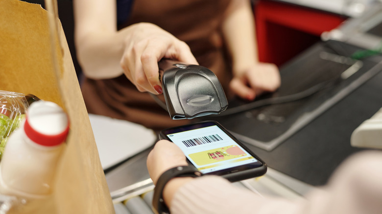 Close up of a customer showing discount code on smartphone screen to cashier at supermarket checkout