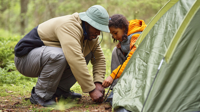 Black man and Black child setting up tent together in forest, crouching and working as team