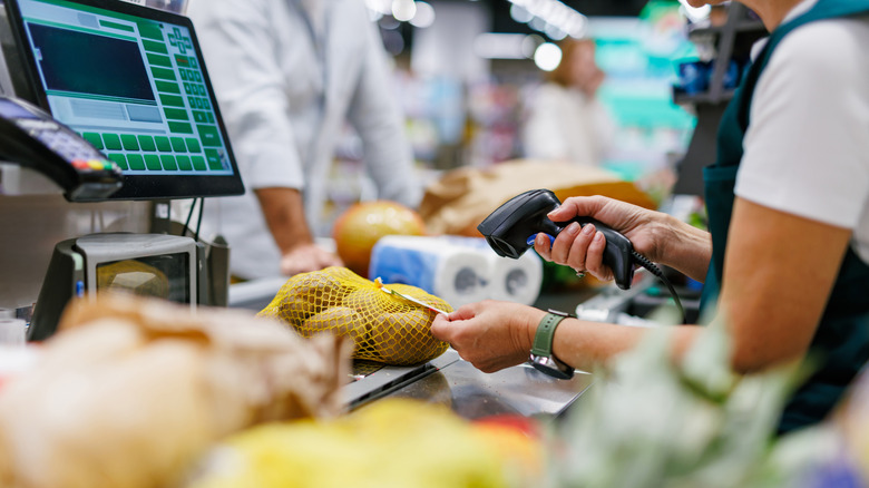 Supermarket cashier scanning potatoes at the checkout, while a customer waits in the background