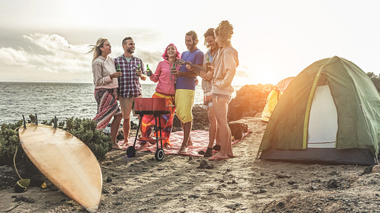 Happy friends camping with a barbecue picnic next to the ocean