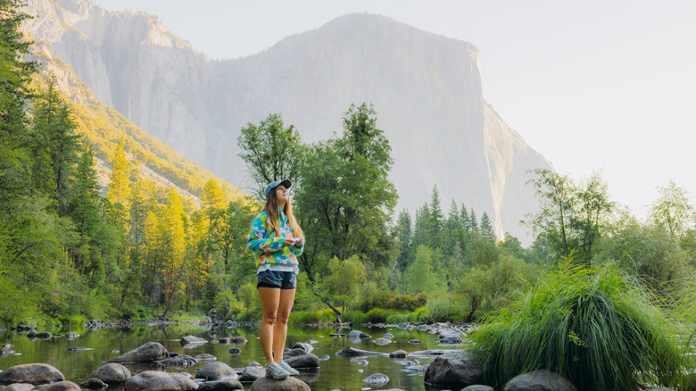 A woman standing on a boulder in a stream with her camera at Yosemite National Park