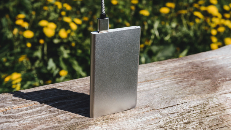 A silver power bank stands vertically on a distressed wooden surface
