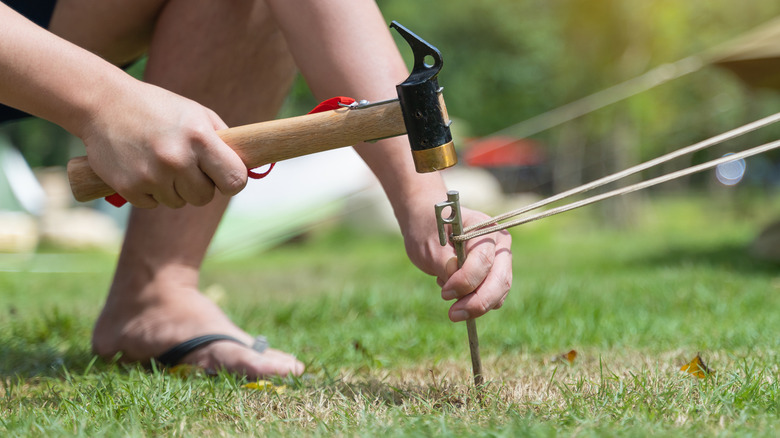 Closeup man hitting a metal tent peg by a hammer into the ground